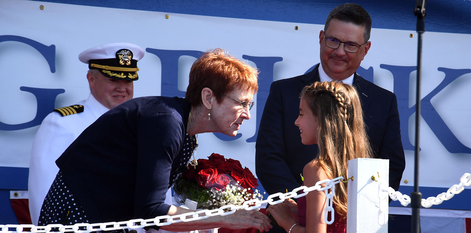Godmother Darleen Greenert (left) presents the granddaughter of a shipyard employee with a flower